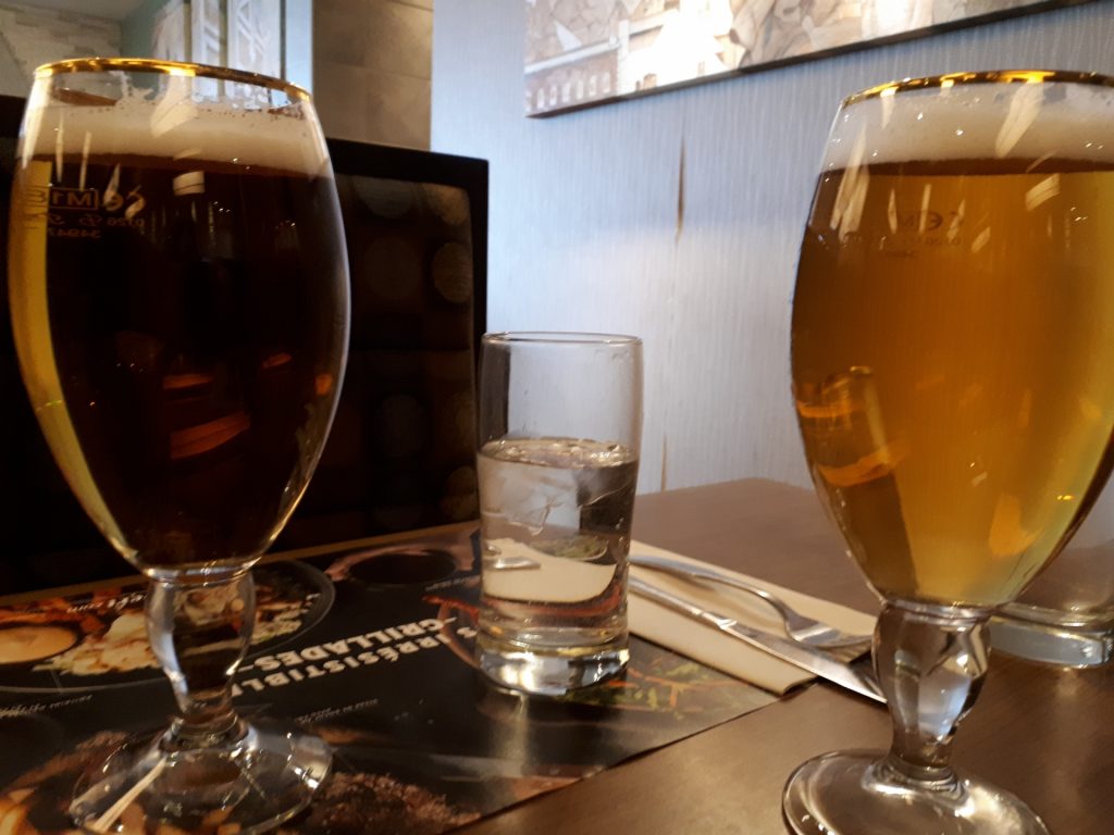 An image of 2 glasses of beer on either side of a glass of water.