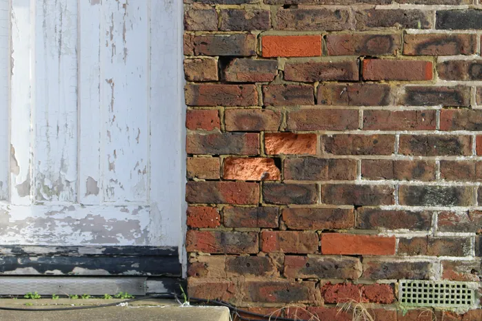 An image of a a brick wall with some bricks being damaged and caved in.